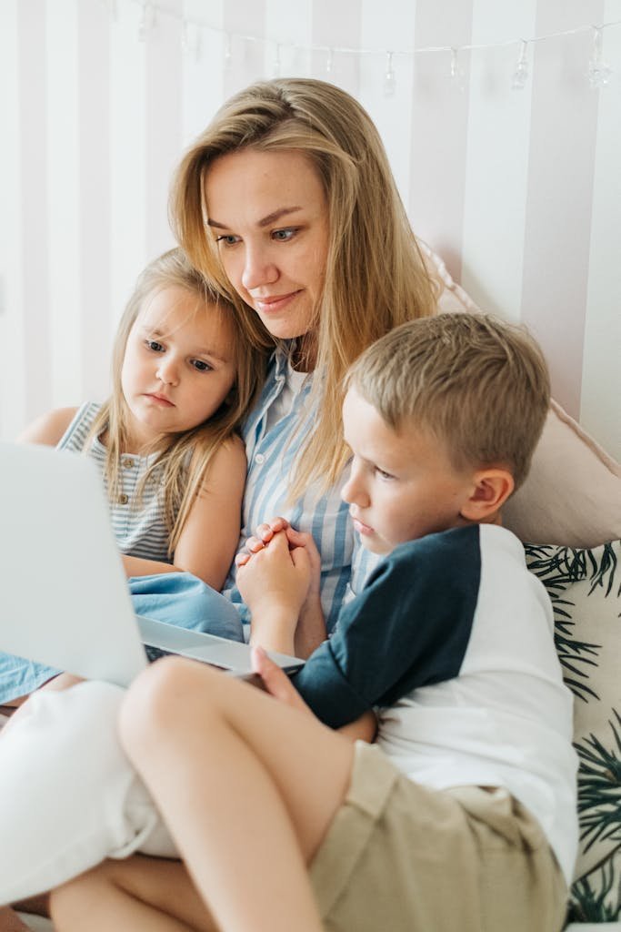 A mother and her children enjoying quality time watching something on a laptop in the bedroom.